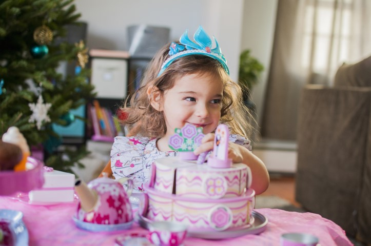 A young girl, resembling the enchanting Snow White, dons a sparkling blue tiara as she gleefully engages with her colorful toy cake set at the dining table. Set against the backdrop of a elegantly adorned Christmas tree, twinkling with beautiful ornaments and glowing lights, this scene exudes holiday magic while highlighting her imaginative play. Perfect keywords: Snow White resemblance, blue tiara, festive atmosphere, toy cake set playtime, beautifully decorated Christmas tree.