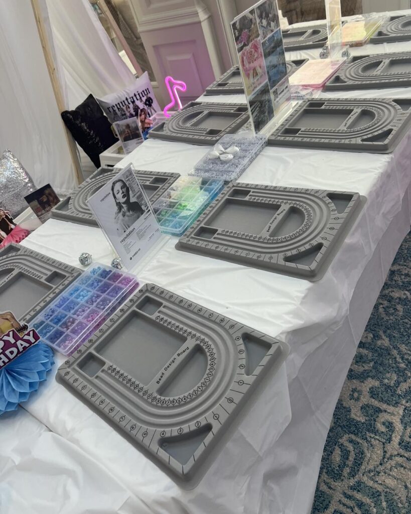 A table is set up with jewelry-making bead boards, containers of colored beads, tools, and instructions—perfect for a fun kids activity.