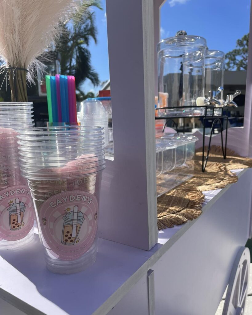 Clear plastic cups with pastel logo designs are stacked on a white cart, next to glass jars, colorful straws, and a pampas grass arrangement—perfect for an outdoor movie night in Florida on a sunny day.